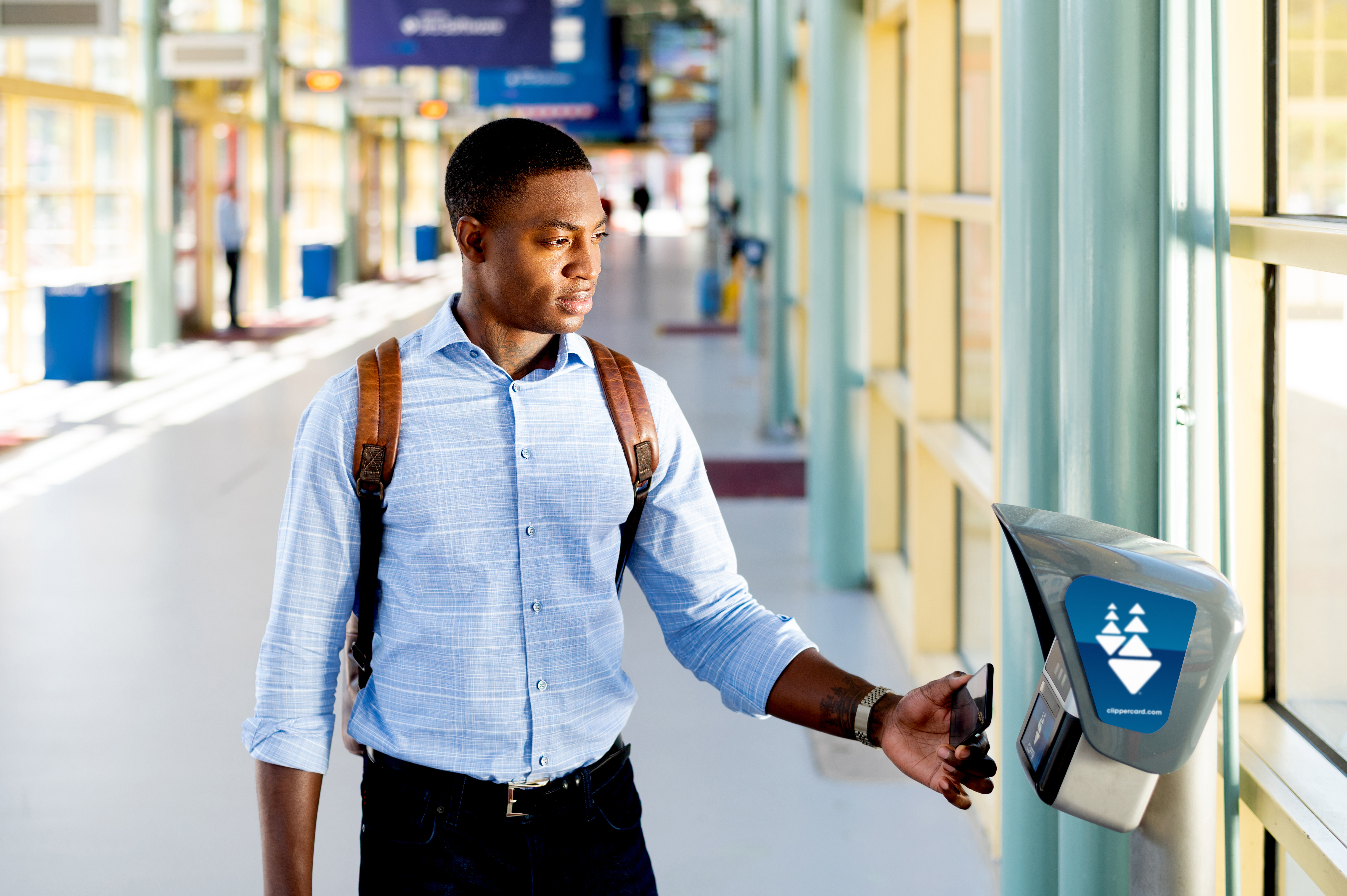 A man in a transit station holds his smartphone up to a Clipper ticket reader