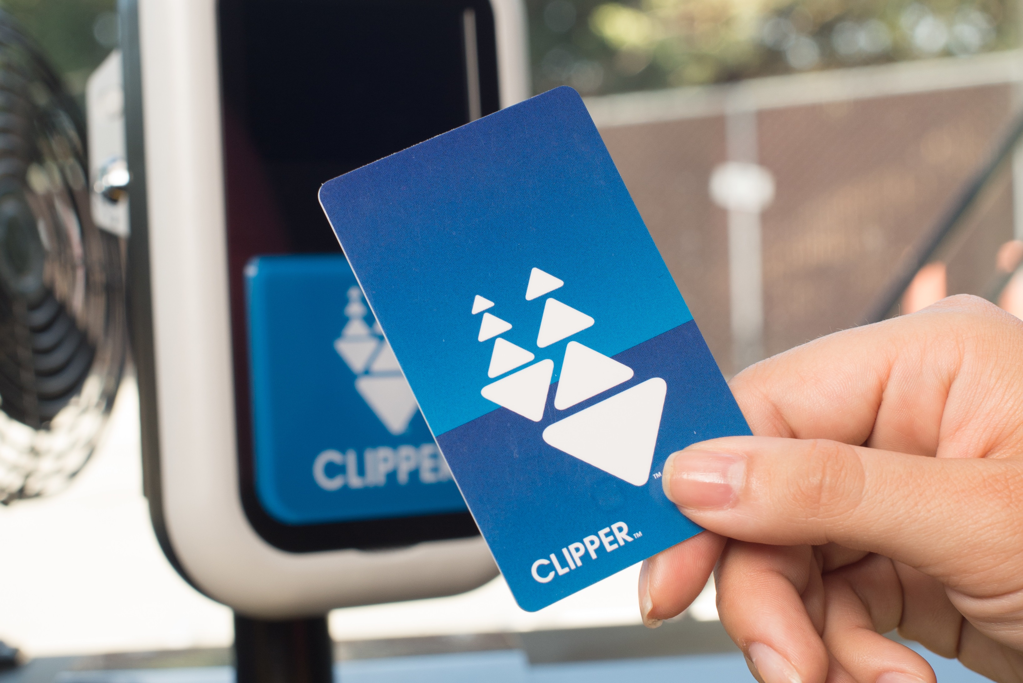 Close-up of a woman’s hand holding a Clipper card over a card reader inside a bus