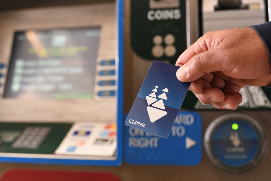 A hand holding up a plastic Clipper card in front of a BART ticket machine