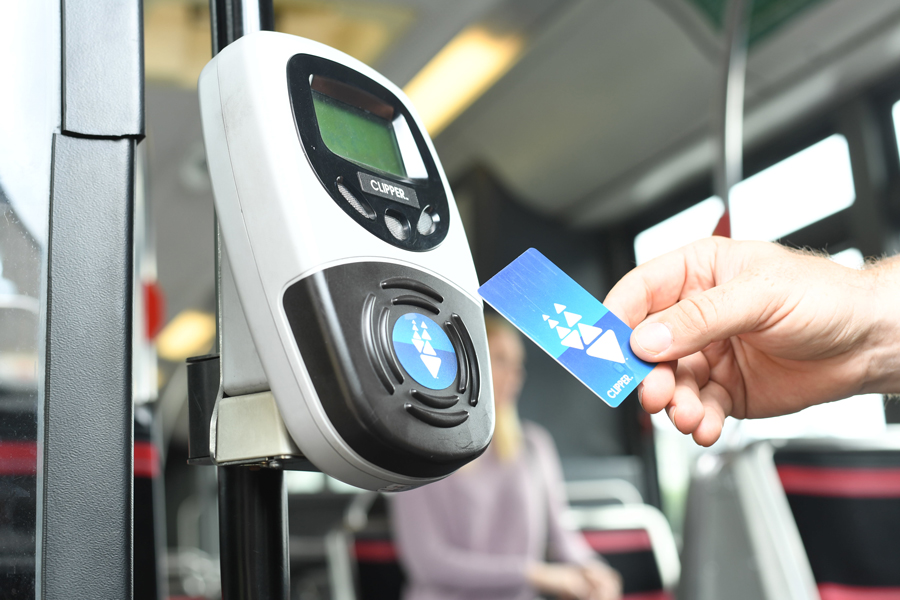 A hand holding a plastic Clipper card up to a ticket reader on an AC Transit bus