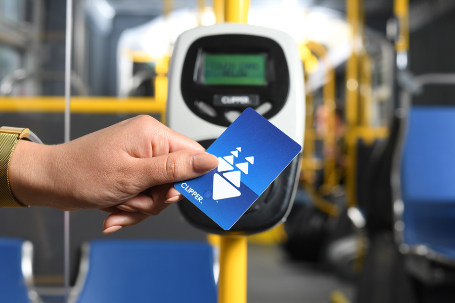 A hand holding a plastic Clipper card up to a ticket reader on a Muni bus
