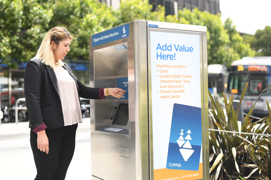A woman standing in front of a Clipper Add Value Machine with a card in hand.
