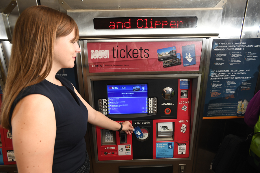 Woman holding a Clipper card over the card reader target of a Muni ticket machine