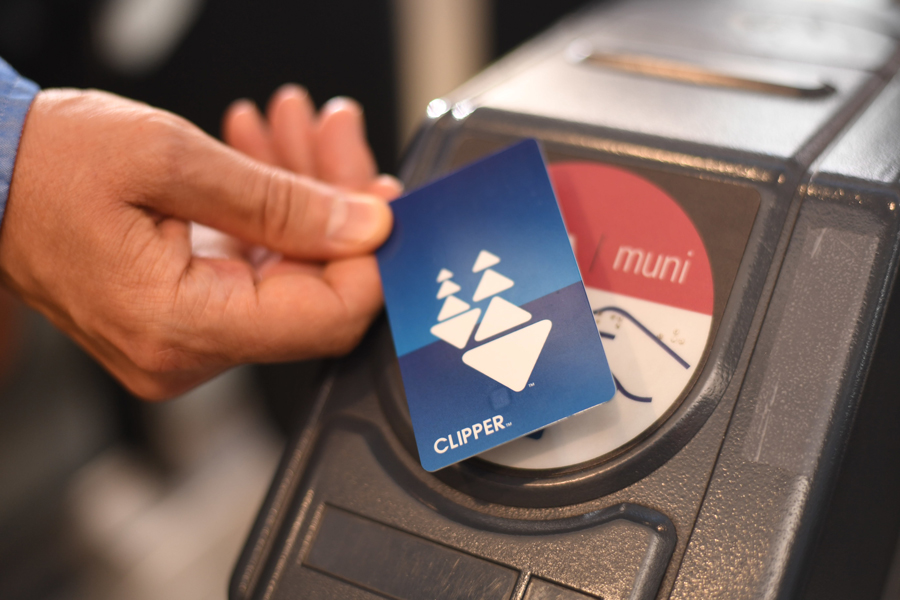 A hand holding a plastic Clipper card tapping a Muni ticket reader