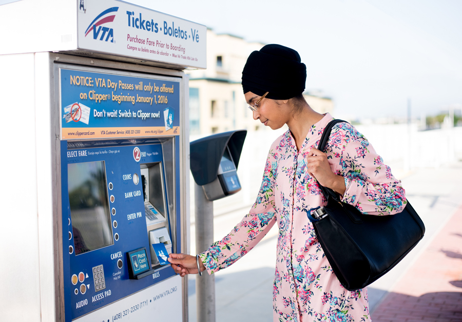A woman standing in front of a VTA ticket machine, holding up her plastic Clipper card to add value