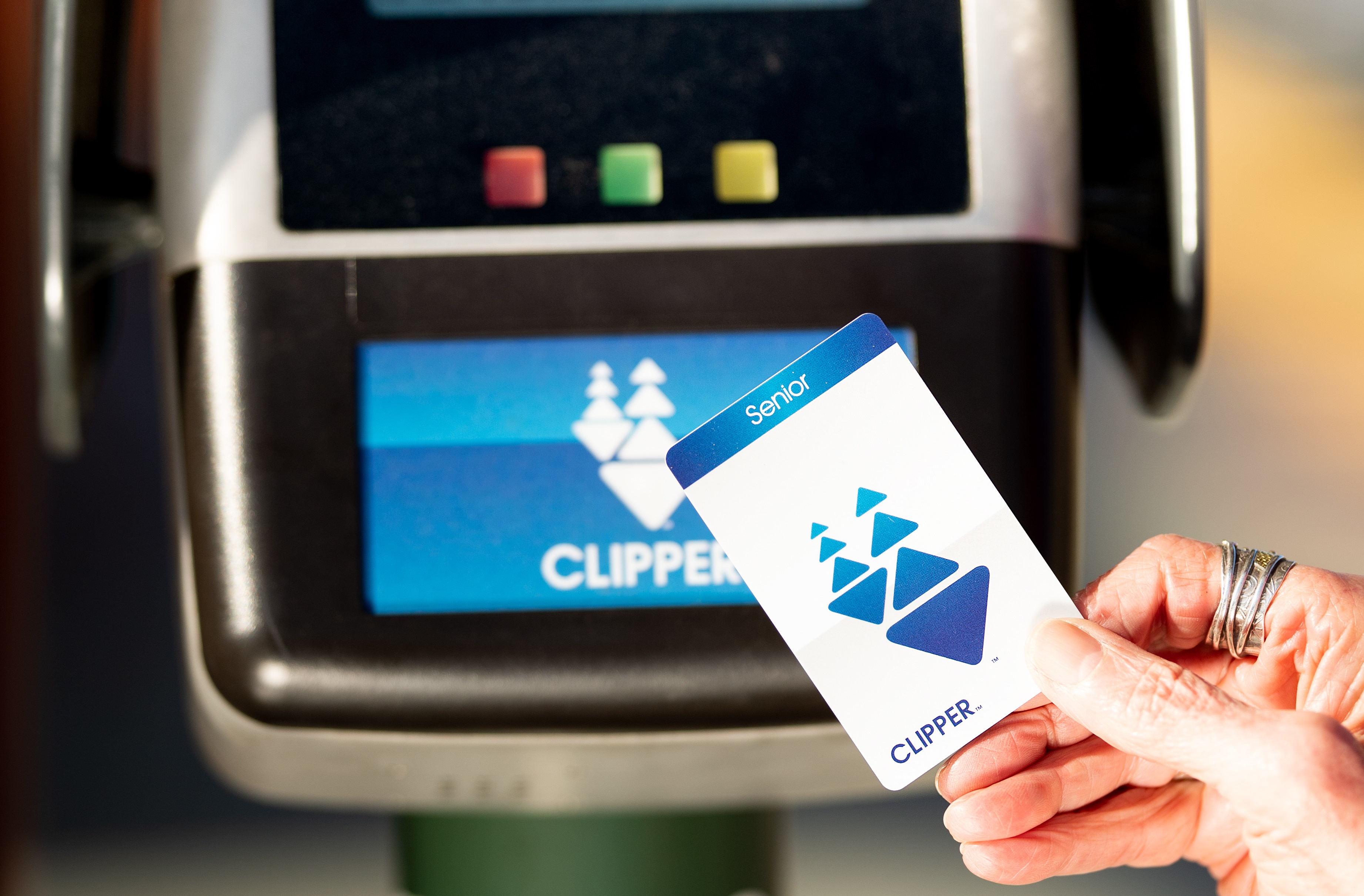 Close-up of a woman’s hand holding a Senior Clipper card over a card reader on a transit platform